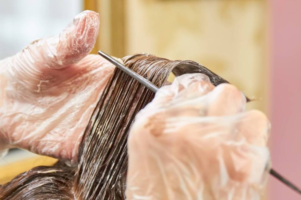 Hands of beautician dyeing hair